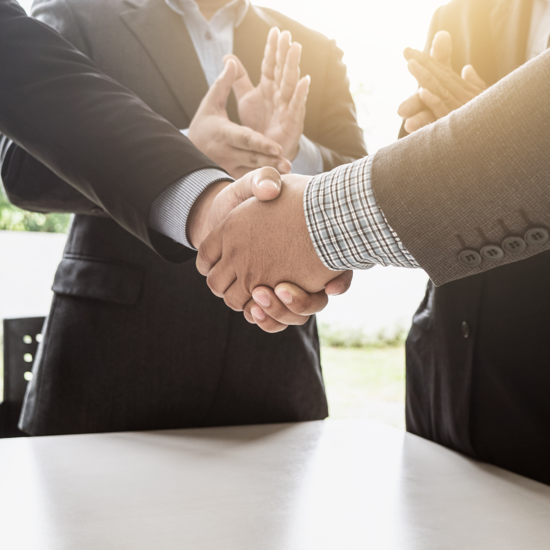Close-up of two business people shaking hands while others applaud representing how Martin Shepherd Solicitors help with joint ventures and partnerships in Potters Bar, Hertford, and Finchley.